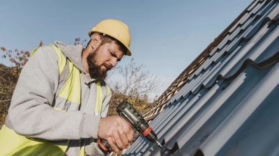 man in a hard hat working on a roof with a power tool