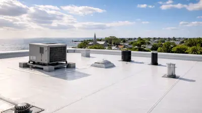 Commercial flat roof with EPDM membrane and HVAC unit overlooking a Rhode Island coastal town under clear skies.