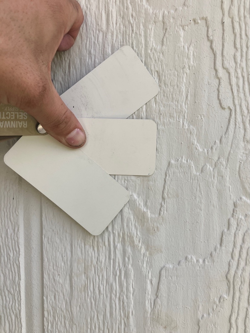 A Mighty Dog Roofing Northern Colorado expert contractor holding color swatches up to a home exterior for comparison. 