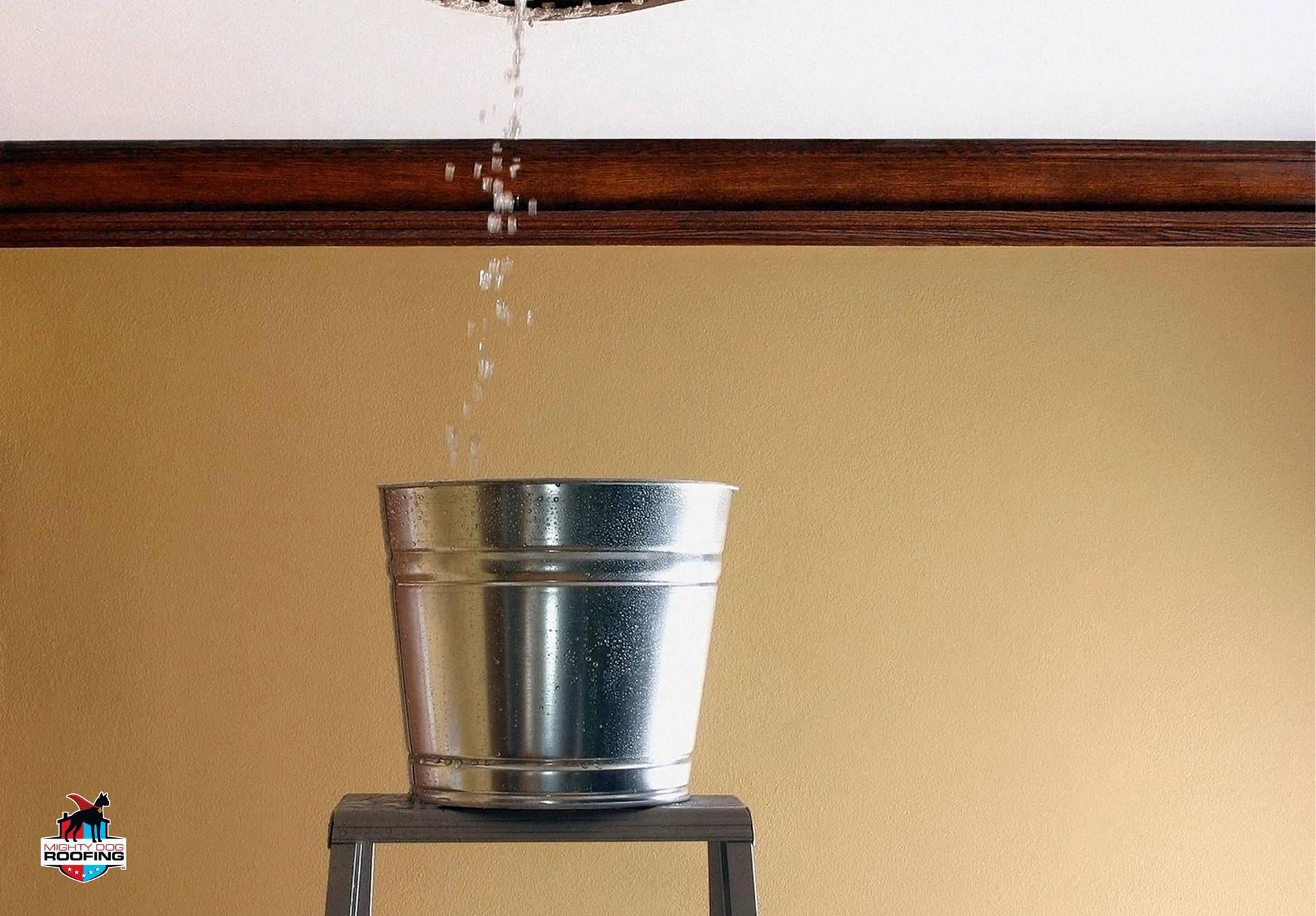 Water leaking through ceiling hole into a metal bucket during an active roof leak